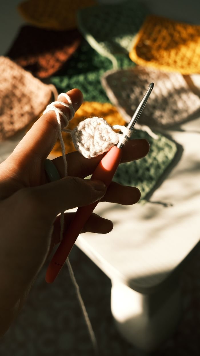 Hand holding crochet hook creating vibrant squares in sunlight.