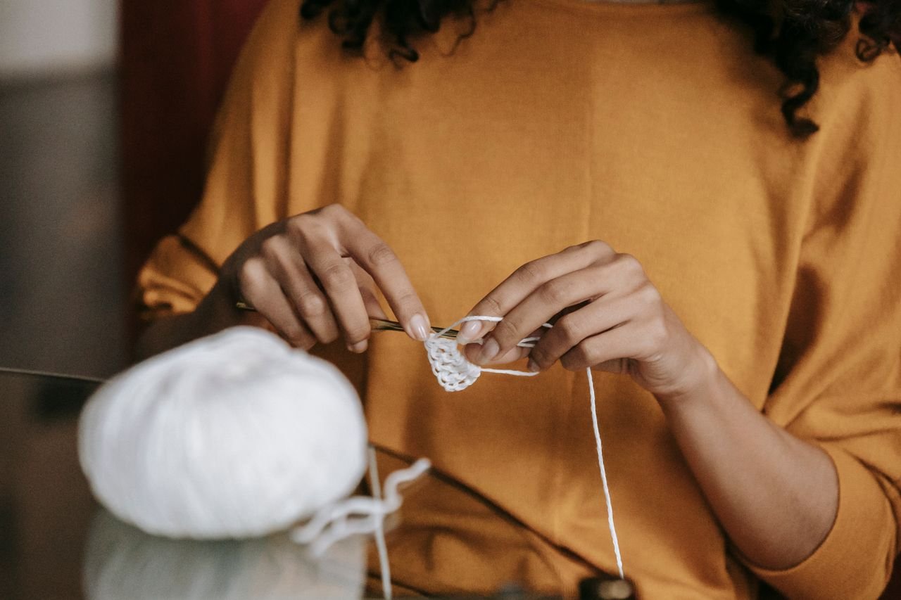 Close-up of a woman crocheting with white yarn, focusing on hands and craftwork.